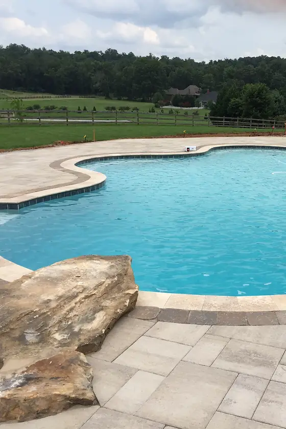A freeform Sequoyah pool with a boulder feature, the Tennessee treeline behind it.